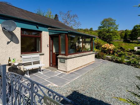A cottage exterior with a white bench and small table on a stone patio at Corner Cottage in Troutbeck