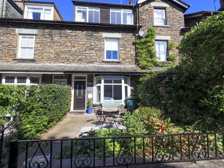 A stone house exterior with black door a bay window garden table and chairs and hedges at Stones Throw Cottage Ambleside