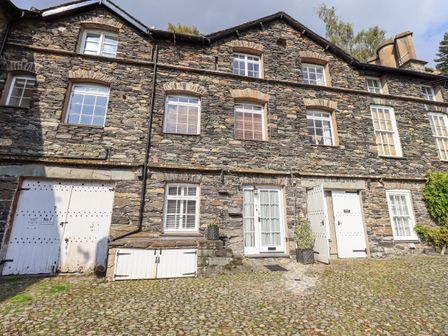 Stone facade of a multi-story building with white doors and windows and cobblestone ground at The Mounting Steps in Ambleside