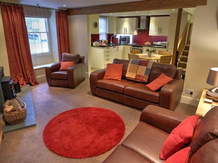 A living room with brown leather sofas and a red round rug next to an open kitchen and dining area at Townfoot Cottage in Langdale