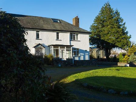 A white two-story house with a slate roof and a chimney surrounded by trees and grass at Grange Fell Borrowdale in Keswick