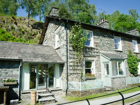 Stone house with white framed windows small garden and hill with trees behind at Oakbank in Langdale