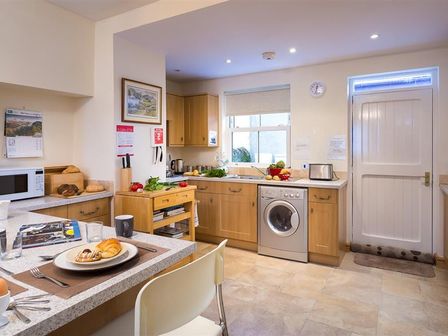 A kitchen with wooden cabinets a washing machine a microwave and a breakfast counter at Mulberry Cottage in Staveley