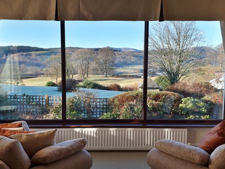 A living room with two armchairs and a large window showing a garden and hills at Lakefield House Hawkshead