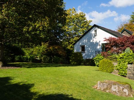 A garden with grass surrounded by trees and shrubs next to a white house at Merewood Lodge in Ambleside