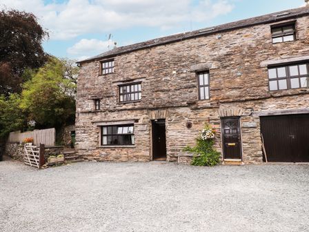 A stone building with multiple windows and doors on a gravel driveway with plants nearby at Cherry Tree Cottage at Satterthwaite in Hawkshead