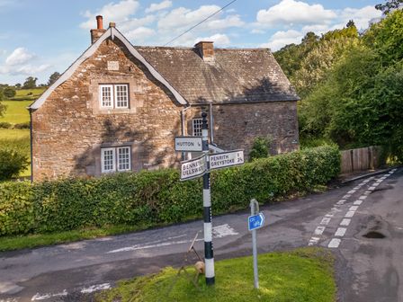 A stone house near a road signpost and hedges at Home Farm House in Penrith