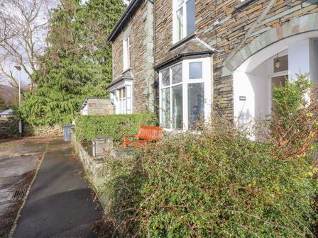 The exterior of a stone house with a bench near a hedge on a sidewalk at Fernleigh Cottage Ambleside