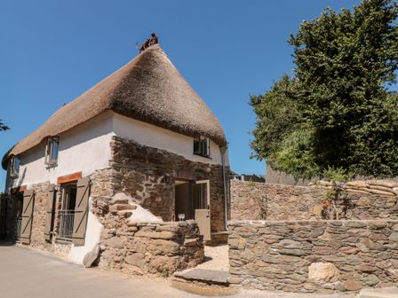 A stone and thatched roof house with wooden shutters and a stone wall outside at The Old Cider Barn in Hope Cove