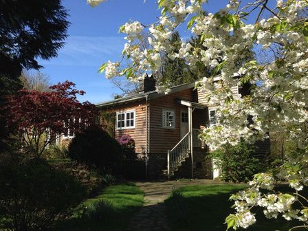 A wooden house surrounded by flowering trees and bushes at Rosewood by the River in Ambleside
