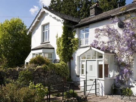 A white cottage with ivy and flowering vines outside and a stone wall in front at The Blithe Hare in Troutbeck Bridge