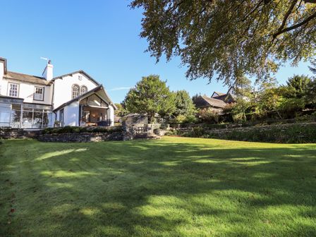A large garden with a lawn and stone terraces outside a white house with large windows at Wykefield in Hawkshead