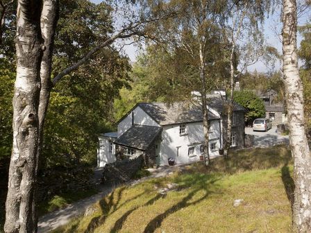 A white house with stone walls and a parked car surrounded by trees and grass at Wythebank in Langdale