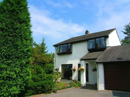 A two story house with white walls garage and green trees around at Fairhaven in Bowness