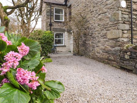 A stone exterior wall of a house with gravel on the ground and pink flowers in the foreground at Buttercup Cottage in Troutbeck