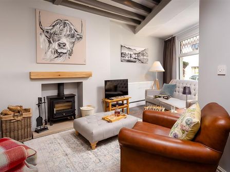 A living room with a wood burner fireplace a leather armchair a grey sofa and a TV at Little Leveret Cottage in Keswick