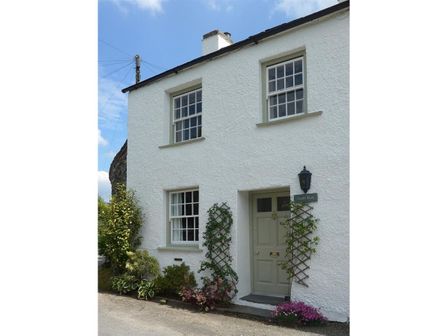A white two story house with green door and windows and plants outside at Croft End Cottage in Sawrey