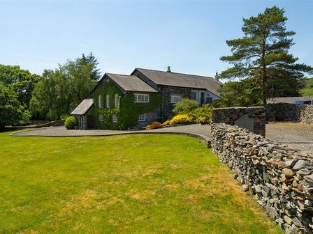 A stone house with ivy-covered walls a gravel driveway and a stone wall with trees surrounding at Bank Barn at Rusland in Grizedale