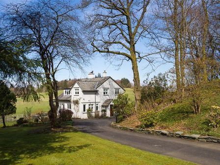 A white two-story house with a driveway surrounded by trees and grass at Juniper Cottage in Windermere