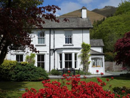 A white two-story house with garden furniture and red flowers in the garden at Ben House in Grasmere