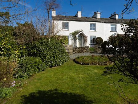 A white cottage with chimneys surrounded by garden and lawn at Birchmill Cottage in Crook