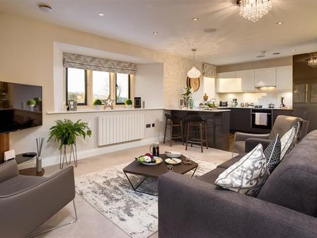 A living room with a gray sofa and armchair a coffee table on a rug and a kitchen with a breakfast bar and stools at Hygge at No8 in Windermere