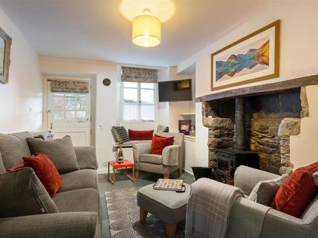 A living room with a stone fireplace a wood stove a television grey sofas with red cushions and a small table at Lettera Ambleside