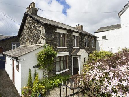 An exterior view of a stone and white painted cottage with plants and flowers at Honeysuckle Cottage in Bowness