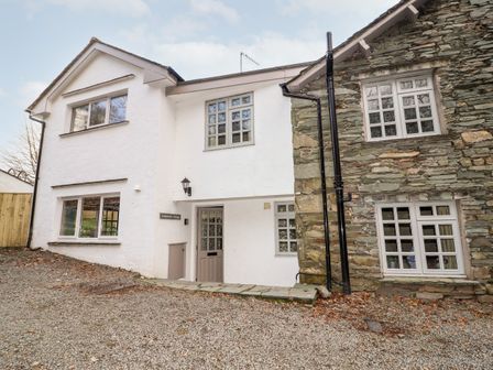 Exterior of a cottage with white and stone walls and multiple windows at Gunpowder Cottage in Langdale