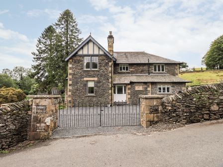 A stone house with multiple windows and a white door behind a metal gate and stone walls at Fair Rigg in Hawkshead