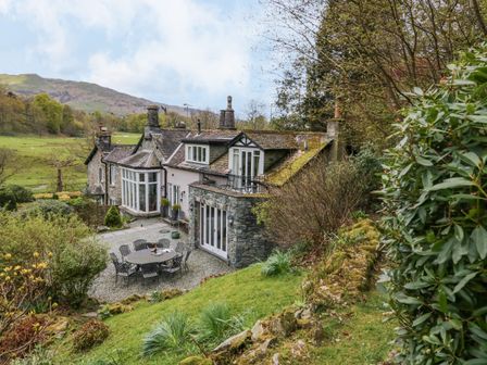 A stone and brick house with outdoor seating area and trees on a hillside at River Lodge in Ambleside