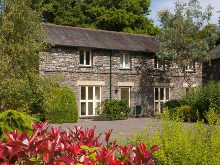 A stone house with multiple windows surrounded by trees and bushes at The Old Barn in Ambleside