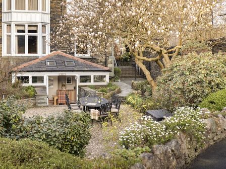An outdoor garden area with a black dining table and chairs under a flowering tree at Archie's in Ambleside
