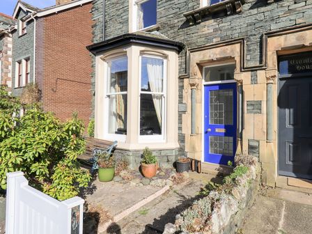 A stone house facade with a blue door a window with curtains potted plants and a bench at Number Twenty in Keswick