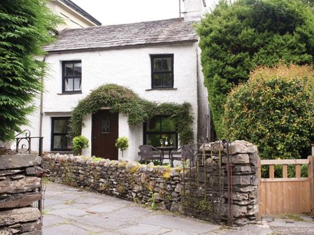A stone walled front garden with patio furniture outside a white cottage Burrow Cottage Bowness