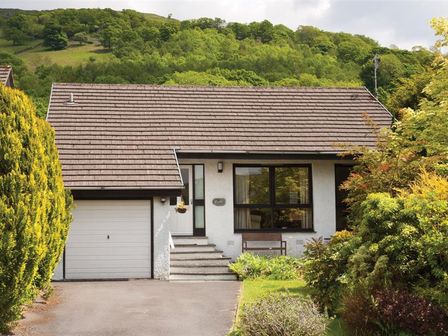 A detached house with a garage and front garden with trees and bushes at Mount Sol in Ambleside