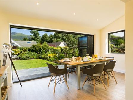 A dining room with a wooden table and four chairs overlooking a garden at Greengarth in Keswick