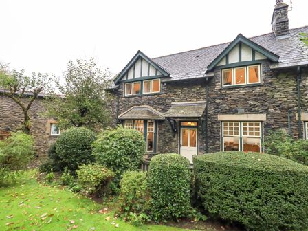 Stone cottage with windows and door surrounded by bushes and trees at Pudding Cottage in Ambleside