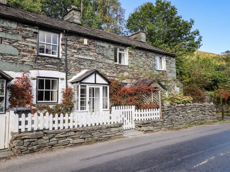 A stone cottage with white framed windows white picket fence and a small porch surrounded by plants and trees at Weir Cottage in Chapel Stile