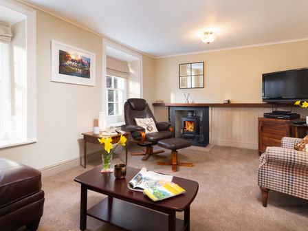A living room with a wood burning stove leather chair coffee table with flowers and a television at Ghyll Foot Cottage in Ambleside