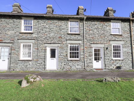 A stone facade row of houses with white doors and windows and green grass in front at Slaters Rest in Langdale