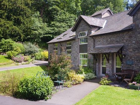 Stone cottage with garden chairs and table surrounded by plants and trees at Gilpin View in Crosthwaite