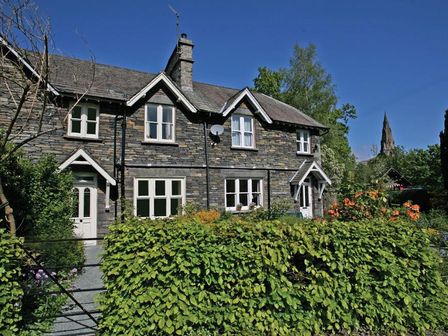 Stone cottage with white framed windows behind green hedge and garden at Rothay Holme Cottage in Ambleside