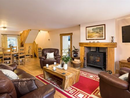 A living room with brown leather sofas a wooden coffee table and a fireplace with a wood stove at Scalegill House in Keswick