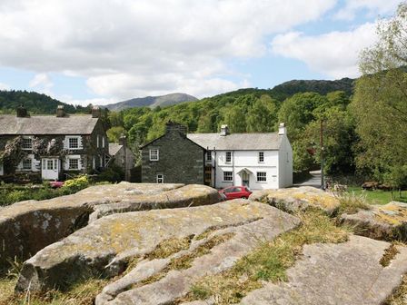 Stone houses with a red car parked between them and large rocks in the foreground at Pollys Cottage in Langdale