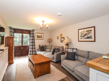 A living room with two gray sofas a wooden coffee table framed pictures and plaid curtains at Candleberry Cottage in Ambleside