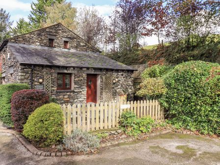 A stone cottage with a wooden fence and various bushes and trees around at Millrace Cottage in Ings