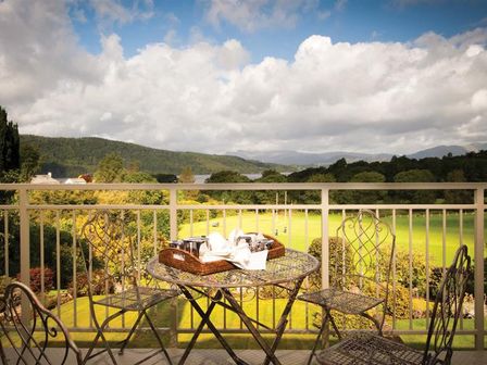 A balcony with a metal table and four chairs overlooking a green field and distant hills at Harrison Stickle in Bowness-On-Windermere