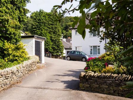A driveway with a gray car and white house surrounded by bushes and trees at Mosslea in Bowness