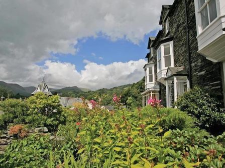 A garden with plants and flowers next to stone houses and hills in the background at Lukes Hoose Ambleside